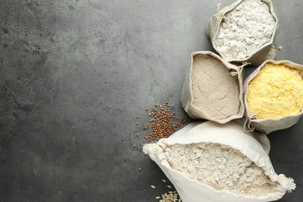 Gri masadaki poşetlerdeki farklı tipte un, düz. Metin için boşluk