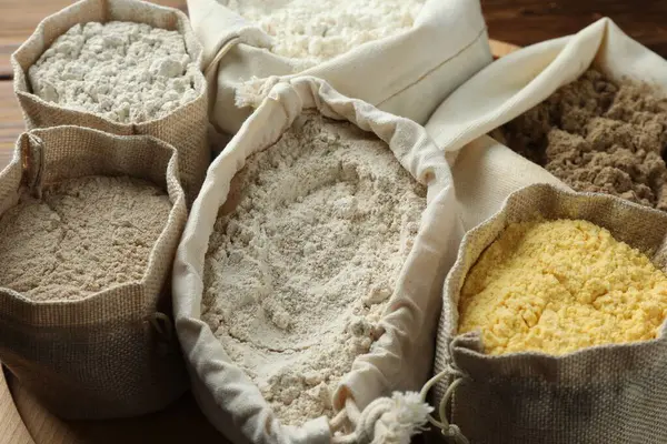 Tahta masadaki poşetlerdeki farklı un türleri, yakın plan.