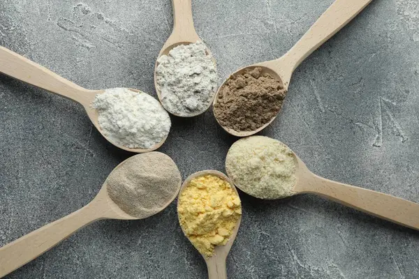 Gri masadaki kaşıklarda farklı türde un, düz.