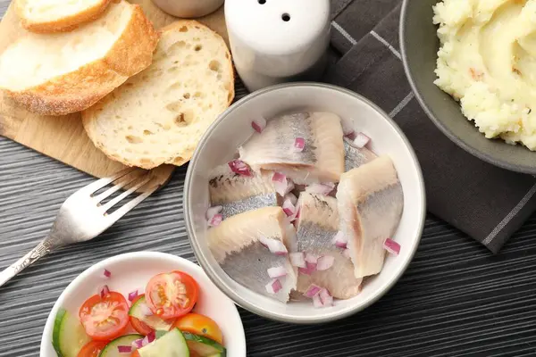 Siyah ahşap masada servis edilen soğanlı lezzetli ringa balıkları.