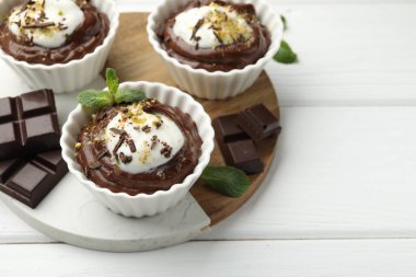 Krem şantili lezzetli puding ve beyaz ahşap masadaki çikolata parçaları, yakın plan. Metin için boşluk