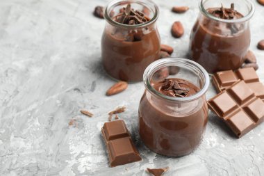 Cam kavanozlarda lezzetli puding, çikolata parçaları ve açık gri masada kakao çekirdekleri, yakın plan. Metin için boşluk