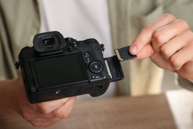 SD bellek kartını masadaki fotoğraf makinesine yerleştiren adam, kapat