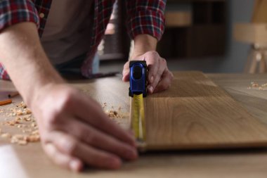 Kapalı alanda bant ile ahşap kalas ölçen bir adam.