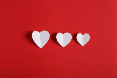 Kırmızı zemin üzerinde beyaz kağıt kalpler, düz uzanmış