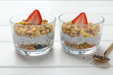 Chia tohumlu lezzetli tatlı, yoğurt, granola ve beyaz ahşap masadaki bardaklarda çilek, yakın plan. Süper yemek.
