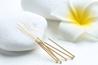 Beyaz arka planda akupunktur iğneleri, spa taşları ve çiçek, yakın plan.