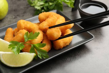 Gri desenli masada tabaktan yemek çubuklarıyla lezzetli tempura karidesleri alıp, yakın plan.