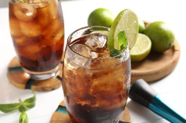 Lezzetli Küba Libre kokteyli bardaklarda, malzemelerde ve beyaz masada, yakın plan.