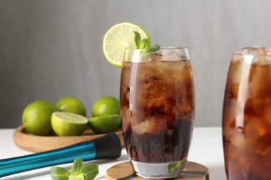 Lezzetli Küba Libre kokteyli bardaklarda, malzemelerde ve beyaz masada, yakın plan.