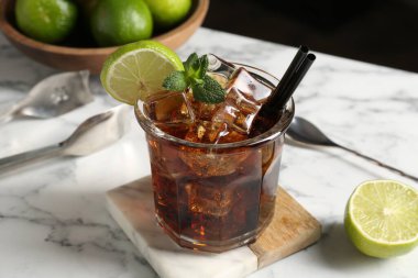 Lezzetli Küba Libre kokteyli, cam, limon, maşa ve kaşıkla beyaz mermer masa, yakın plan.