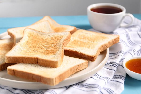 ломтики вкусного жареного хлеба и варенья на светло-голубом столе на сером фоне, крупным планом