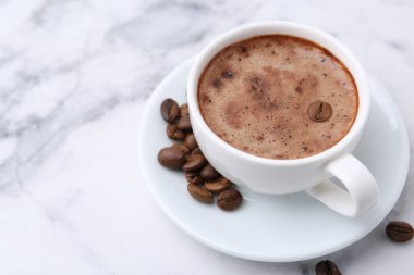 Aromatik kahve fincanda, fasulye ve çay tabağı beyaz mermer masada, yakın plan. Metin için boşluk