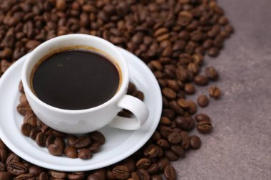 Kahve fincanda, çay tabağında ve kahve çekirdeği kahverengi desenli masada, yakın plan.