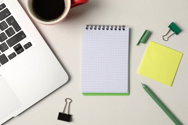 Not defteri, yapışkan not, kalem, cilt klipsleri, kahve ve dizüstü bilgisayar beyaz masada, düz yerde.