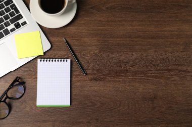 Defter, kalem, yapışkan not, bardaklar, kahve ve dizüstü bilgisayar ahşap masada, düz konum. Metin için boşluk