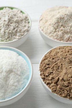 Beyaz ahşap masadaki kaselerdeki farklı un türleri, yakın plan.