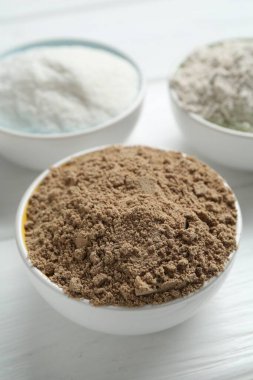 Beyaz ahşap masadaki kaselerdeki farklı un türleri, yakın plan.