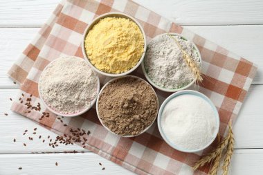 Beyaz ahşap masada farklı tipte un, çivi ve keten tohumu var.