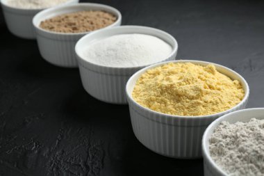 Siyah desenli masa üzerindeki kaselerde farklı un türleri, yakın plan.