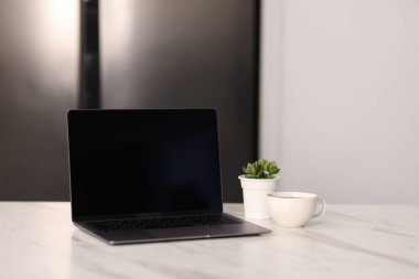 Boş ekranlı dizüstü bilgisayar, bir fincan sıcak içecek ve mutfaktaki beyaz mermer masa üzerinde ev bitkisi. Tasarım için model