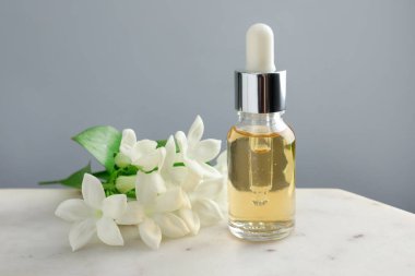 Yağ şişesi ve yasemin çiçekleri gri arka planda, yakın plan