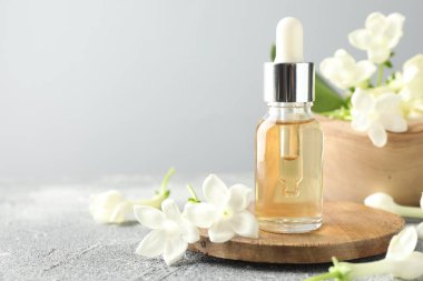 Bir şişe yağ ve yasemin çiçeği gri masada, yakın plan. Metin için boşluk