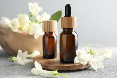 Yağ şişeleri ve yasemin çiçekleri gri masada, yakın plan.