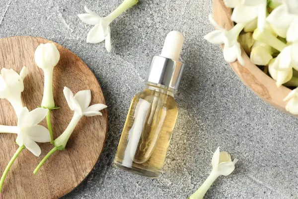 Bir şişe temel yağ ve yasemin çiçekleri gri masada, düz yatıyordu.