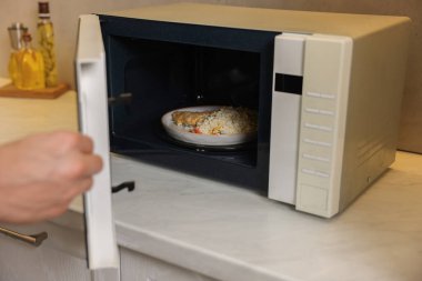 Yemek tabağını mikrodalgaya koyan adam, yakın plan.