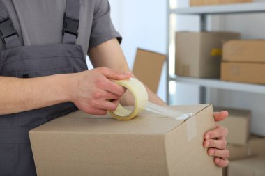 Kapalı alanda yapıştırıcı bantlı karton kutu mühürleyen adam.