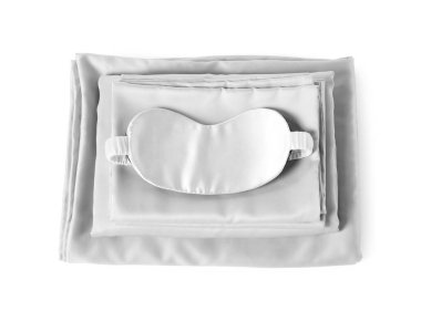 Beyaz arka planda ipeksi çarşaf ve uyku maskesi yığını.