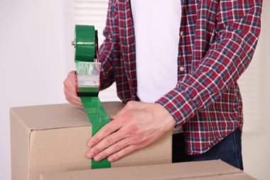 Karton kutuyu kapalı bir yere kapatmak için yapıştırıcılı bant kullanan bir adam.