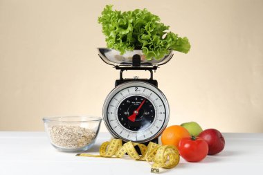 Ürünlerle birlikte mekanik mutfak terazisi ve bej arka planda beyaz ahşap masadaki şerit. Diyet