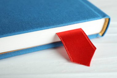 Beyaz ahşap masa üzerinde kırmızı kurdele yer imi olan kitap, yakın plan.