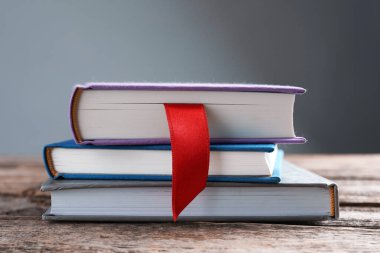 Kırmızı kurdele yer imi ve ahşap masadaki renkli kitap gri arkaplanda, yakın plan