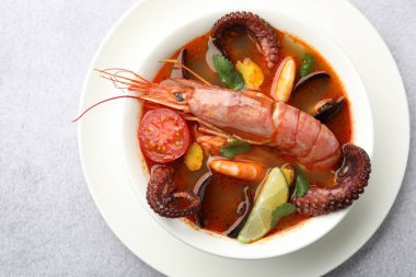 Açık gri masada, tabakta leziz deniz ürünleri çorbası.