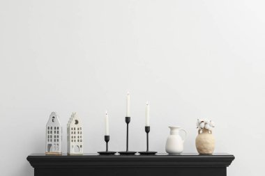 Beyaz duvarın yanındaki şöminede yanan mumlar ve diğer dekorlarla süslü şamdanlar.