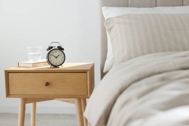 Alarmlı komodinli komodin, bir bardak su ve yatağın yanında kitap.
