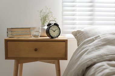 Yatağın yanında kitaplar, vazoda çiçekler, çalar saat ve yatağın yanında bir bardak su.