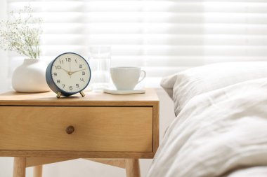 Çalar saati olan bir komodin, vazoda çiçekler, yatağın yanında bir bardak su, yakın plan.