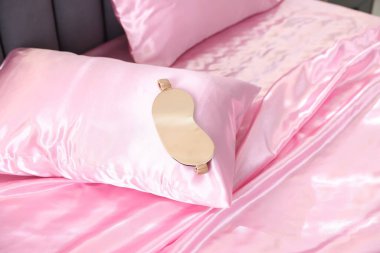 Lüks pembe ipek çarşaflar ve yatakta uyku maskesi.