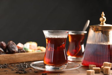 Geleneksel Türk çayı cam fincanlar, çaydanlık, kuru yapraklar, kahverengi şeker ve tatlılar ahşap masada, yakın plan