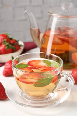 Aromatik meyve çayı, çilek ve nane şekeri beyaz masada, yakın plan.
