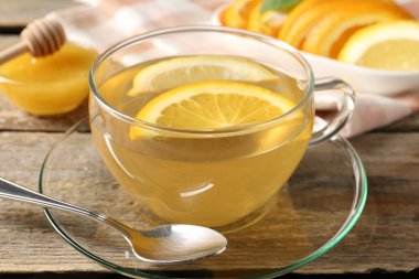 Cam fincanda aromatik meyve çayı, portakal, limon ve bal ahşap masada, yakın plan.