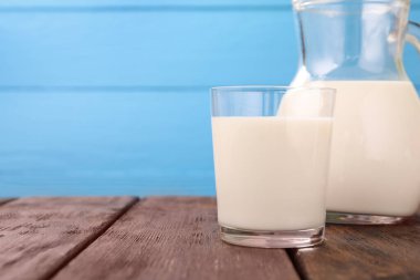 Açık mavi arka plana karşı ahşap masada taze süt, yakın plan. Metin için boşluk