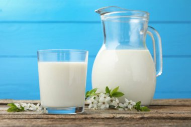 Taze süt ve çiçekler ahşap masada açık mavi arka planda, yakın plan