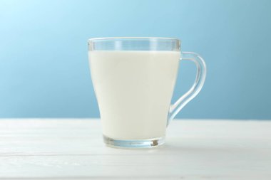 Cam bardaktaki taze süt beyaz ahşap masada açık mavi arka planda, yakın plan