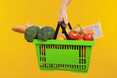 Sarı arka planda farklı ürünleri olan alışveriş sepeti tutan adam, yakın plan.