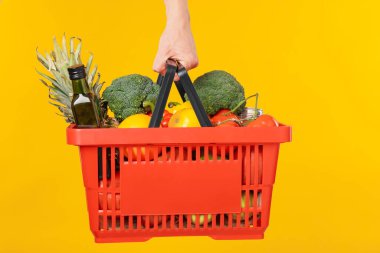 Sarı arka planda farklı ürünleri olan alışveriş sepeti tutan adam, yakın plan.